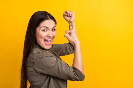 Profile side photo of charming nice happy young woman raise fists winner isolated on shine yellow color backgroundの写真素材