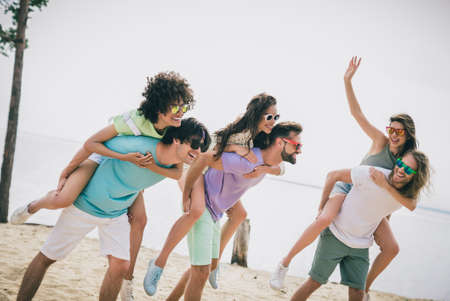 Photo of overjoyed cheerful friends piggyback ride enjoy hanging out sand beach outdoorsの写真素材