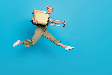 Full body photo of funky young blond lady jump with bag wear t-shirt overall shoes isolated on blue...