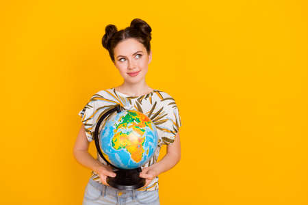 Photo of thoughtful sweet woman wear print t-shirt holding globe looking empty space isolated yellow color backgroundの写真素材