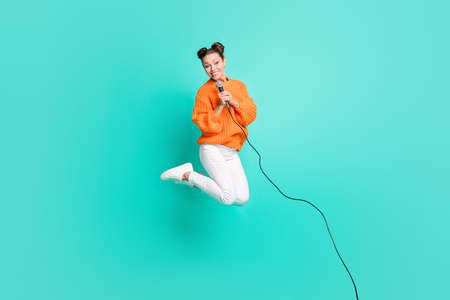 Full size photo of young beautiful smiling positive cheerful girl jumping singing in mic isolated on teal color backgroundの写真素材