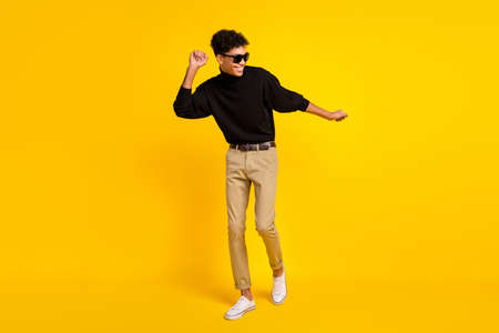 Photo of funky sweet dark skin man wear black sweater eyewear dancing isolated yellow color backgroundの写真素材