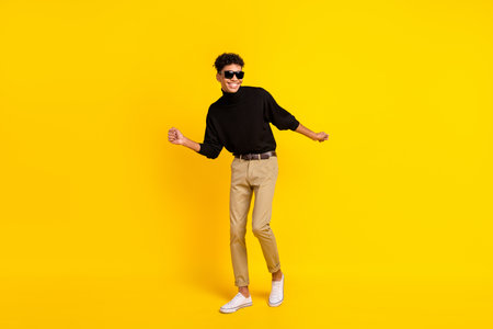 Full size photo of optimistic nice brunet guy dance wear spectacles black sweater trousers sneakers isolated on yellow backgroundの写真素材