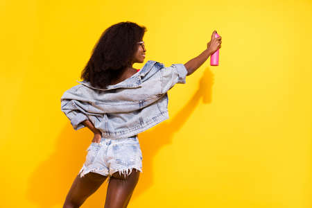 Back rear spine view photo of afro american woman paint wall spray street artist isolated on yellow color backgroundの写真素材