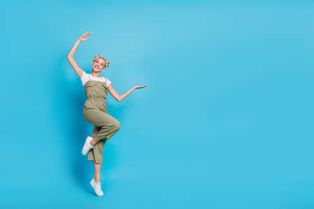 Full length photo of funky young lady jump index promo wear t-shirt overall footwear isolated on...