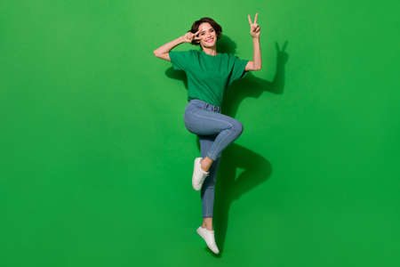 Photo of pretty sweet lady wear spring outfit showing v-signs cover eye jumping high isolated green color backgroundの写真素材