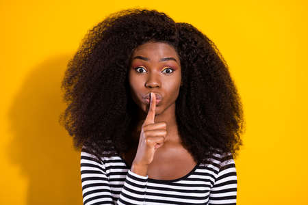 Photo portrait of young woman keeping finger near lips secret gossiping isolated bright yellow color backgroundの写真素材