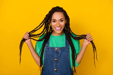 Portrait of cheerful pretty lady hands hold hairdo tails toothy smile isolated on yellow color backgroundの写真素材