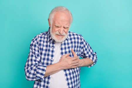 Picture of old pensioner grandfather touching chest suffering from heart attack isolated on teal color backgroundの写真素材