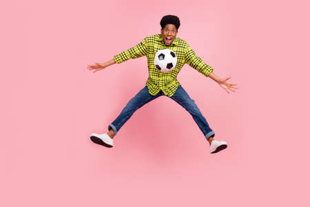Full size photo of young cool brunette guy jump with ball wear shirt jeans sneakers isolated on pink...