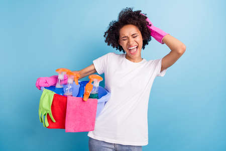 Photo of young angry stressed african girl in white t-shirt screaming overworked cleaning isolated on blue color backgroundの写真素材