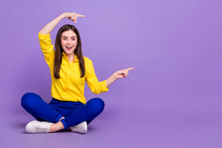 Portrait of attractive cheerful girl sitting demonstrating copy empty space ad solution isolated over bright violet purple color backgroundの写真素材