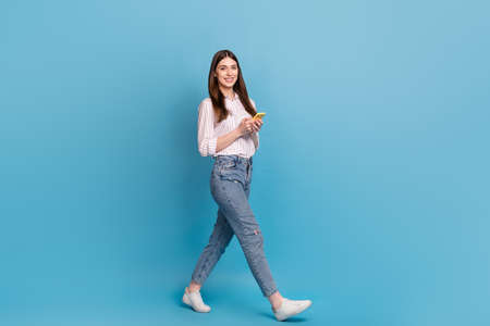 Full length body size view of attractive cheerful trendy girl using gadget strolling isolated over bright blue color backgroundの写真素材