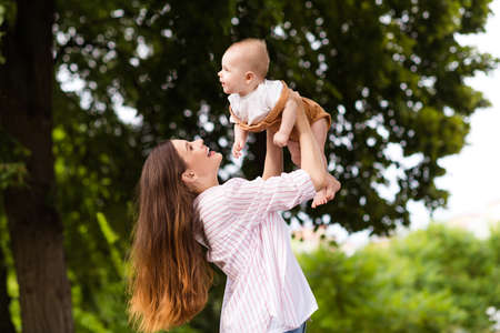 Photo of excited cheerful mother little son dressed casual clothes rising arms enjoying sunshine outdoors backyardの写真素材