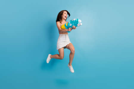 Full size profile side photo of young girl happy positive smile play water gun jump isolated over...