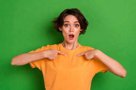 Photo of shocked funky young lady wear orange outfit pointing fingers herself open mouth isolated green color backgroundの写真素材