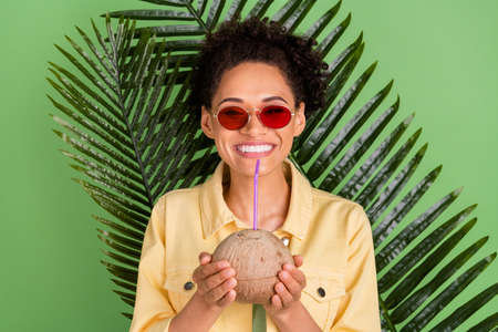 Photo of funky millennial brunette lady hold coconut wear yellow shirt eyewear isolated on green...