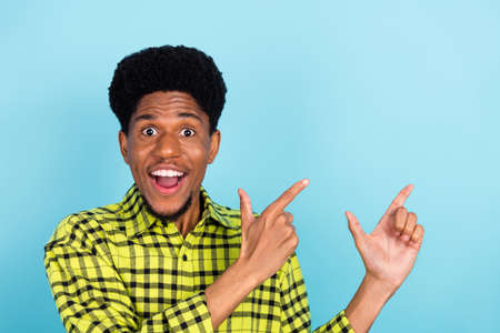 Photo of millennial brunette impressed guy point empty space wear yellow shirt isolated on blue color backgroundの写真素材