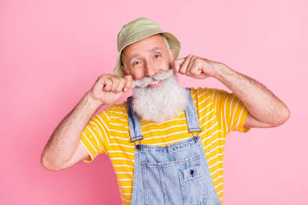 Portrait of attractive cheerful funky man touching beard good mood isolated over pink pastel color...