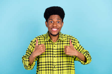 Photo of young brunette funky guy thumb up wear yellow shirt isolated on blue color backgroundの写真素材