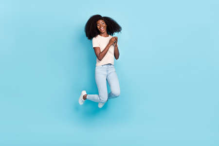 Full size photo of excited active attractive girl jump hands hold telephone isolated on blue color...
