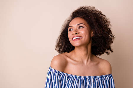 Photo of adorable positive girl toothy smile look interested empty space isolated on beige color...