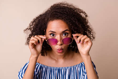 Photo of impressed cute lady wear striped outfit arm dark glasses big eyes isolated beige color backgroundの写真素材