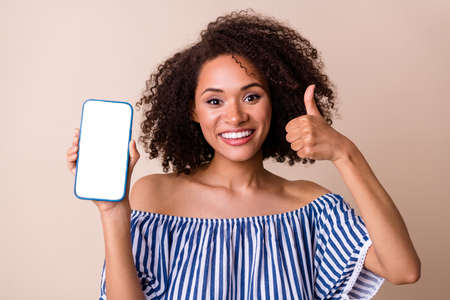 Photo of attractive charming person show thumb up empty space telephone display isolated on beige...