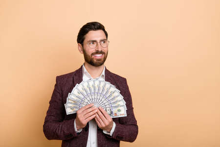 Photo of handsome businessman look empty space see shopping promo hold fan of money isolated on beige color backgroundの写真素材