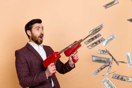 Photo of young shocked amazed surprised businessman with money gun see shopping promo isolated on beige color backgroundの写真素材