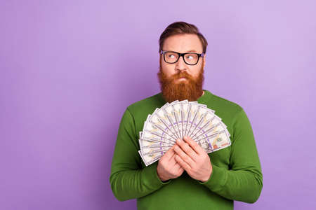 Portrait of young attractive wealthy male brainstorming hold lots of money fan of dollars isolated on purple color backgroundの写真素材