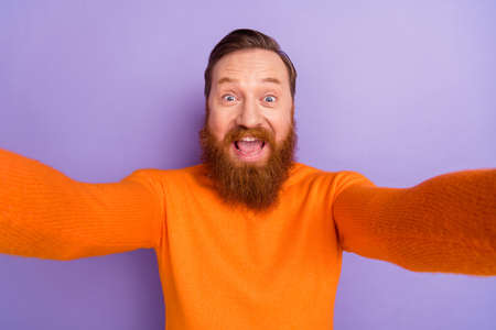 Photo of laughing crazy foxy man blogger take selfie making video from his trip isolated on violet color backgroundの写真素材