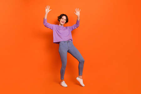 Full length photo of funny adorable girl dressed purple pullover dancing empty space isolated orange...
