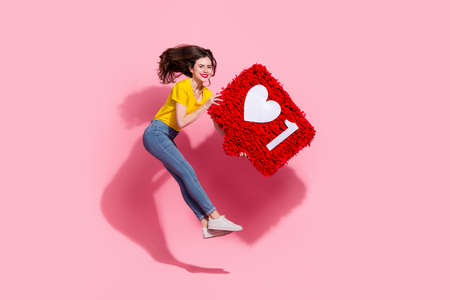 Full length photo of impressed young brunette lady jump with pinata wear t-shirt jeans shoes isolated on pink backgroundの写真素材