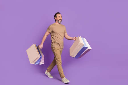 Full body photo of mature funky man go do shopping look promo wear t-shirt trousers footwear isolated on purple backgroundの写真素材