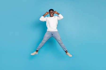 Full length portrait of astonished cheerful man jump hands touch eyeglasses isolated on blue color...