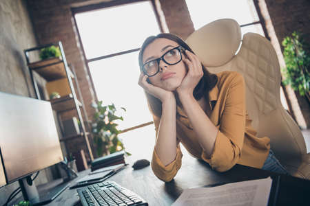 Portrait of unsatisfied minded girl arms cheekbones sitting chair workplace office building inside