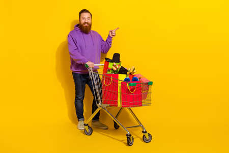 Full body photo of cheerful handsome man indicate finger empty space offer promo isolated on yellow color backgroundの写真素材