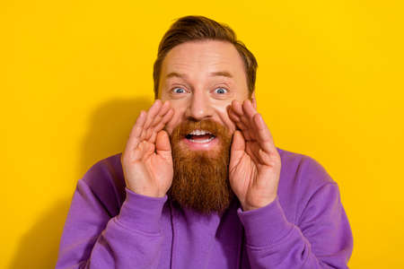 Photo of positive cheerful man wear violet sweatshirt arms lips making announcement isolated yellow color backgroundの写真素材