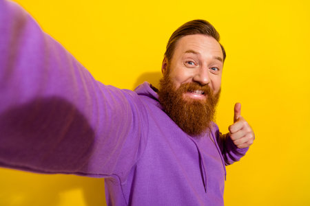 Portrait of good mood attractive male take selfie shooting himself blogger show thumb-up isolated on yellow color backgroundの写真素材