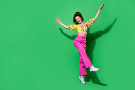 Full length photo of cute charming girl dressed off shoulders top jumping high walking empty space isolated green color backgroundの写真素材