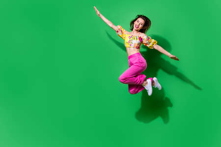 Full length photo of dreamy childish girl dressed off shoulders top jumping high arms sides empty space isolated green color backgroundの写真素材