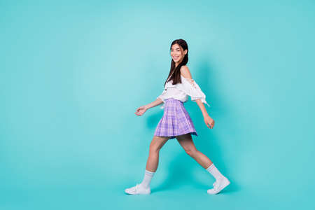 Full body profile photo of adorable positive filipino girl walking empty space isolated on teal color backgroundの写真素材