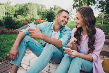 Photo of dreamy pretty boyfriend girlfriend wear casual outfits showing modern gadget sitting stairs enjoying sunny weather outdoors gardenの写真素材