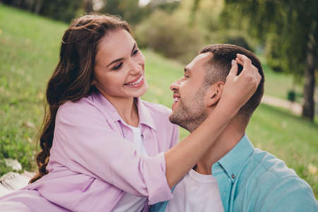 Photo of charming cheerful young wife husband dressed pastel shirts sitting green grass cuddling enjoying sunshine outdoors backyardの写真素材