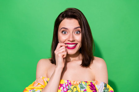 Portrait of nice cheerful person biting finger nail toothy beaming smile isolated on green color backgroundの写真素材