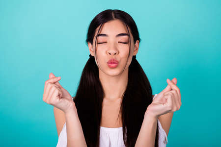 Photo of adorable nice thai lady closed eyes kiss lips fingers show love symbol isolated on vivid cyan color backgroundの写真素材