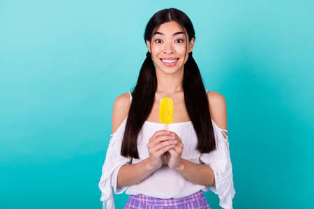 Photo of positive pretty lovely lady holding summer season refreshing fruity popsicle isolated cyan color backgroundの写真素材