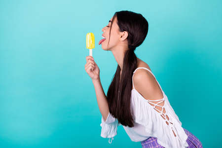 Profile side photo of cute lovely lady lick yummy cold fruit juice frozen yogurt pop isolated cyan color backgroundの写真素材