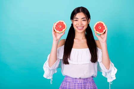 Photo of cheerful positive lady wear white rising two orange halves empty space isolated turquoise color backgroundの写真素材